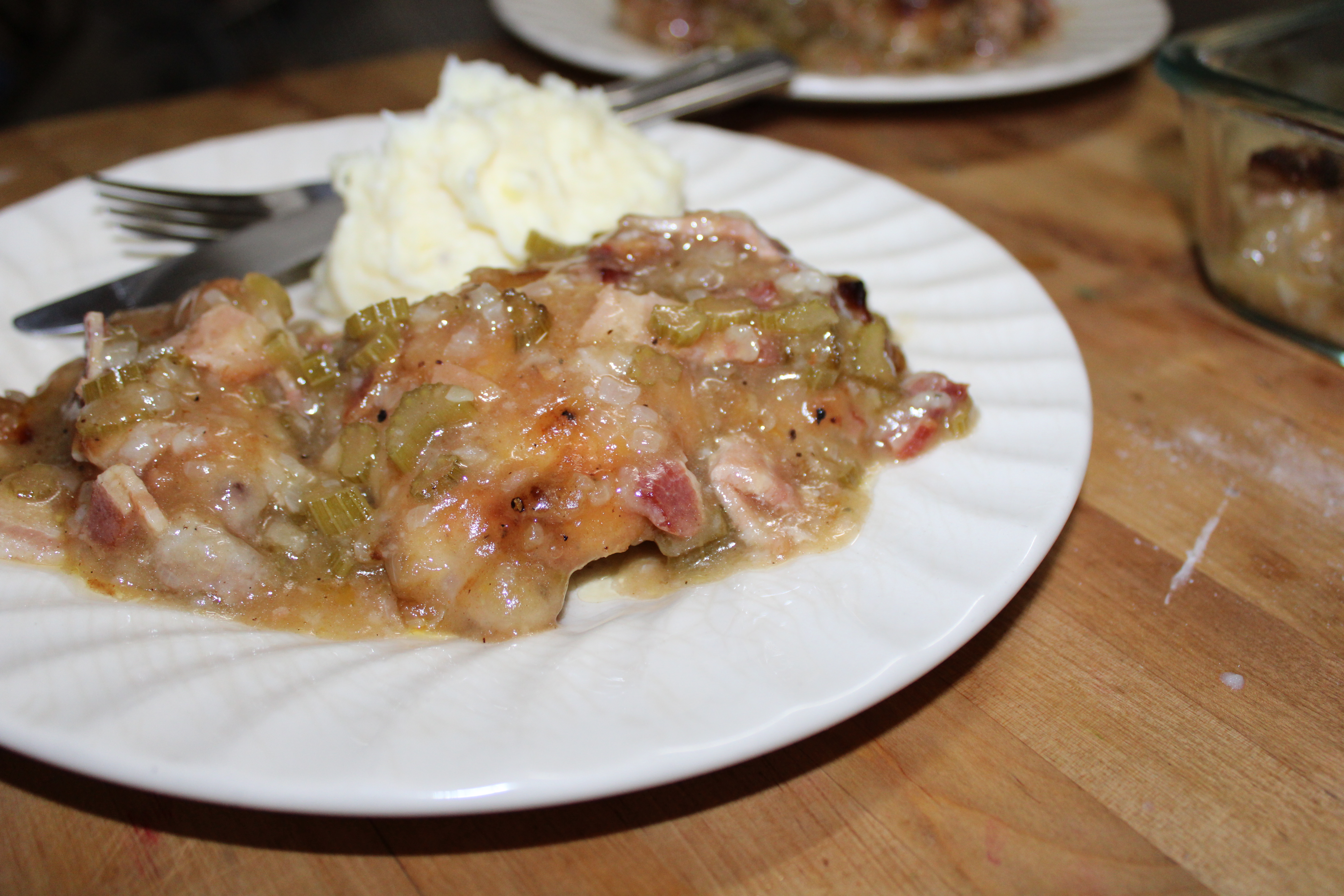 Casserole and mashed potatoes on a cream plate with cutlery on a timber bench