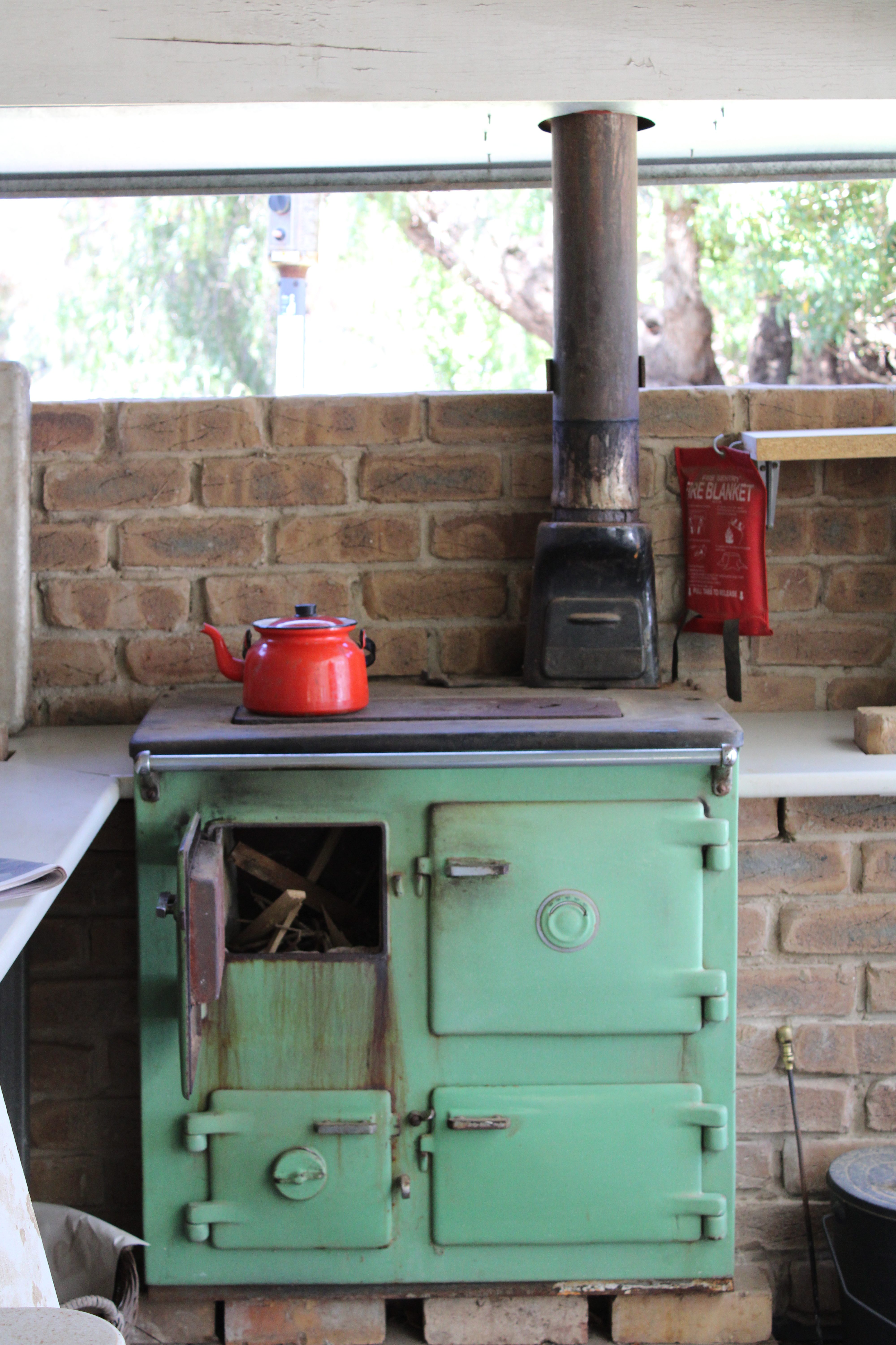 Wood burning oven installed with shelving, fire ready to light, kettle on stove top