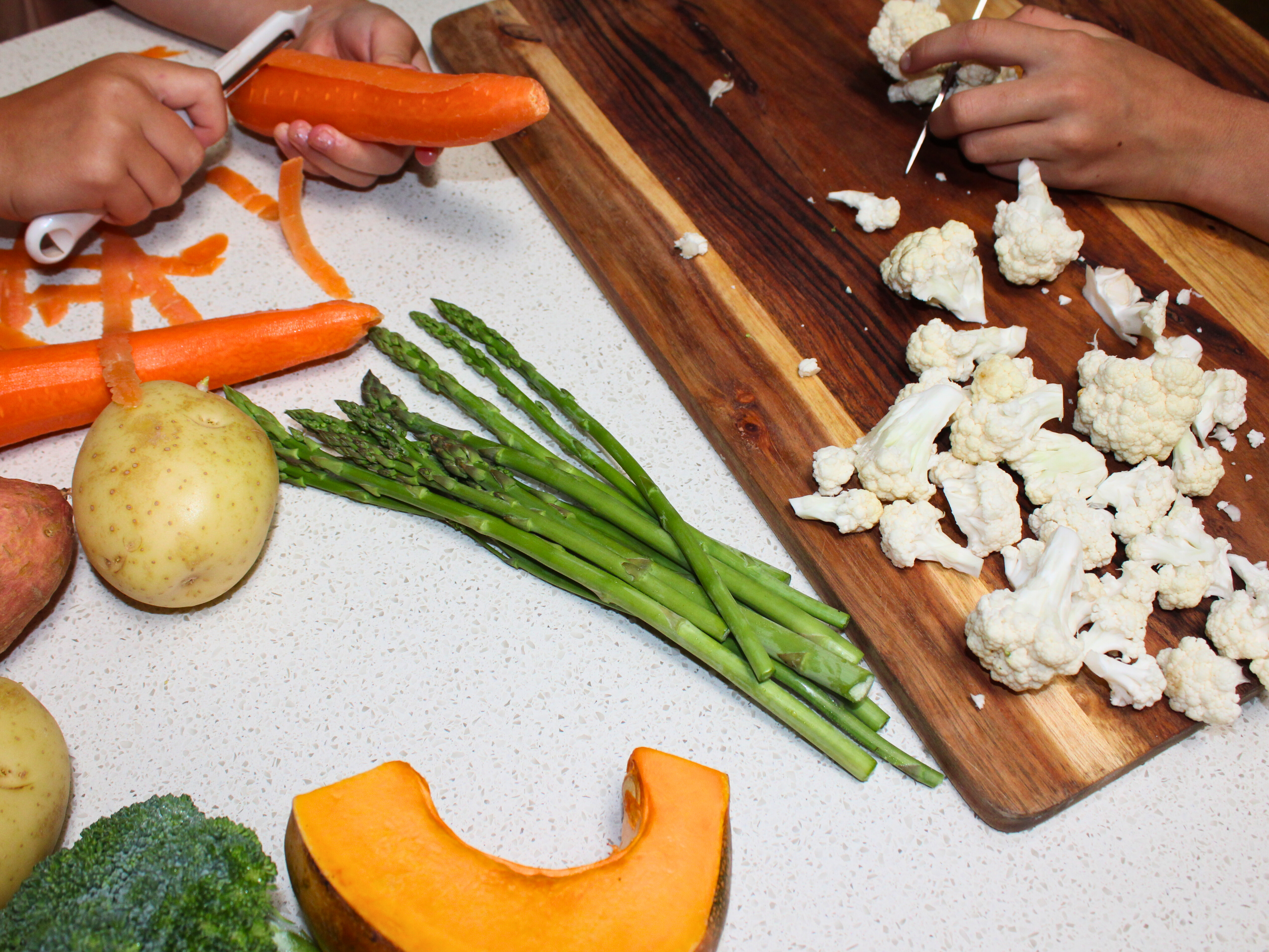 Vegetables on a bench with a cutting board, peeler and knife